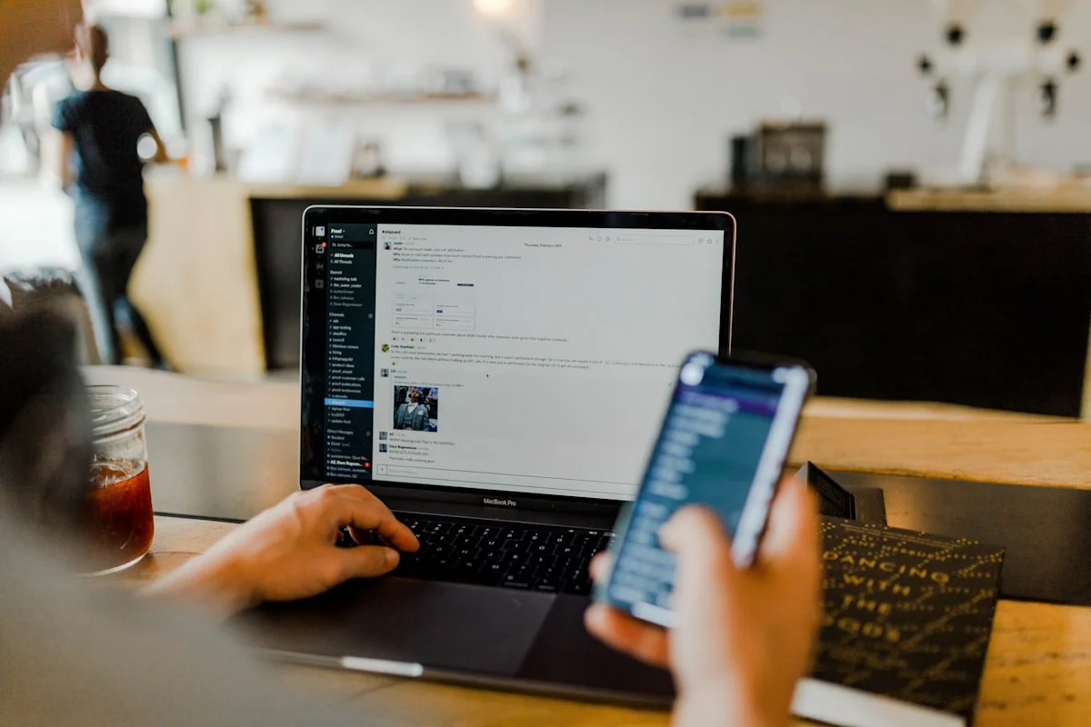A phone held in one hand beside an open laptop at a counter